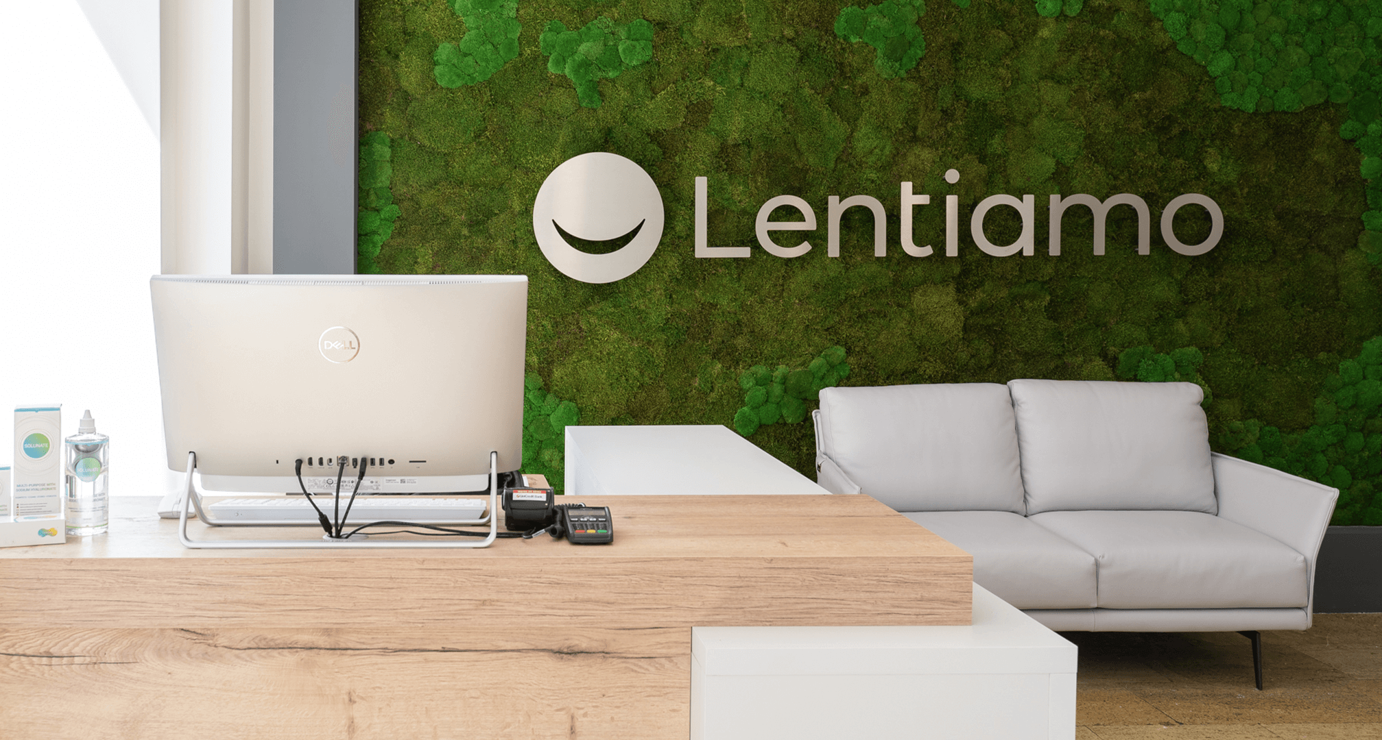 silver computer monitor in front of green moss wall with silver lentiamo sign